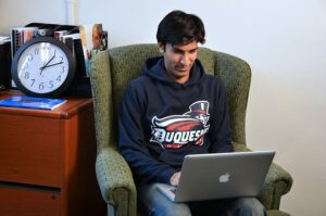 A Duquesne student on a computer sitting in a chair.