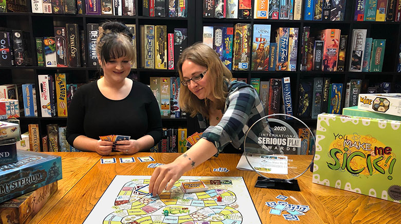 Partnership in Education team members Brinley Kantorski (left) and Sarah Will play You Make Me Sick, an award-winning game that teaches players about infectious diseases.