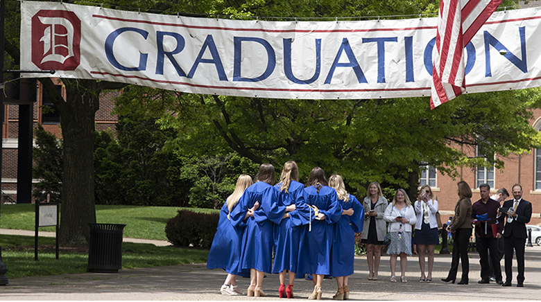 recent graduates pose for photo under Graduation banner