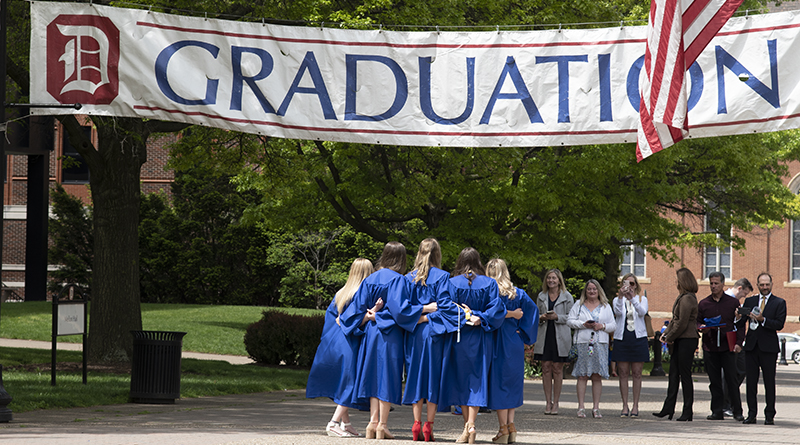 recent graduates pose for photo under Graduation banner
